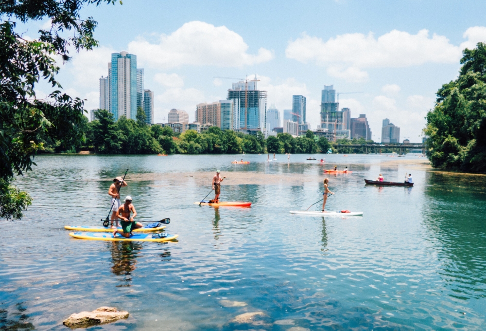 Photo of SUP - Stand Up Paddleboarders - on Lady Birdy Lake in Austin, Texas, with the Austin skyline in the background. This is one activity that is part of the Heywood Hotel Austin Summer Staycation Package.